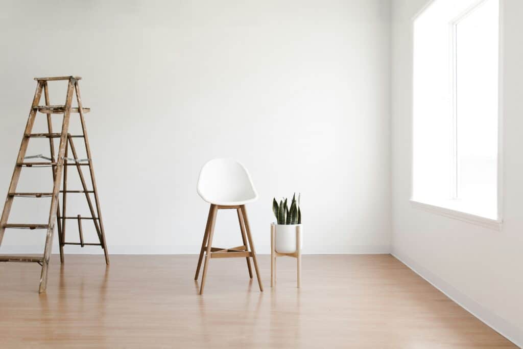 Empty room with a wooden step ladder, white chair and a potted snake plant on a light wood floor