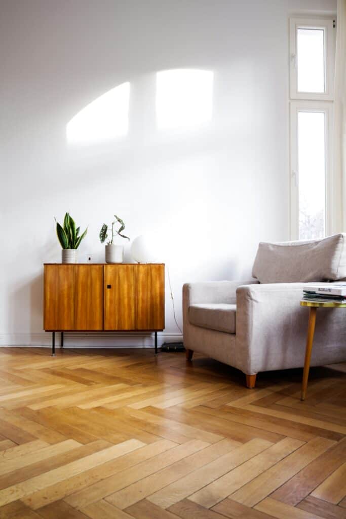 Sunlight falling across a herringbone parquet floor beside a wooden sideboard and armchair