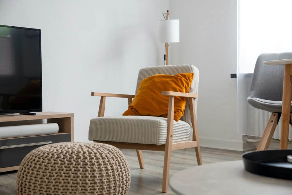 Living room corner with a wooden-framed armchair, orange cushion and knitted pouffe