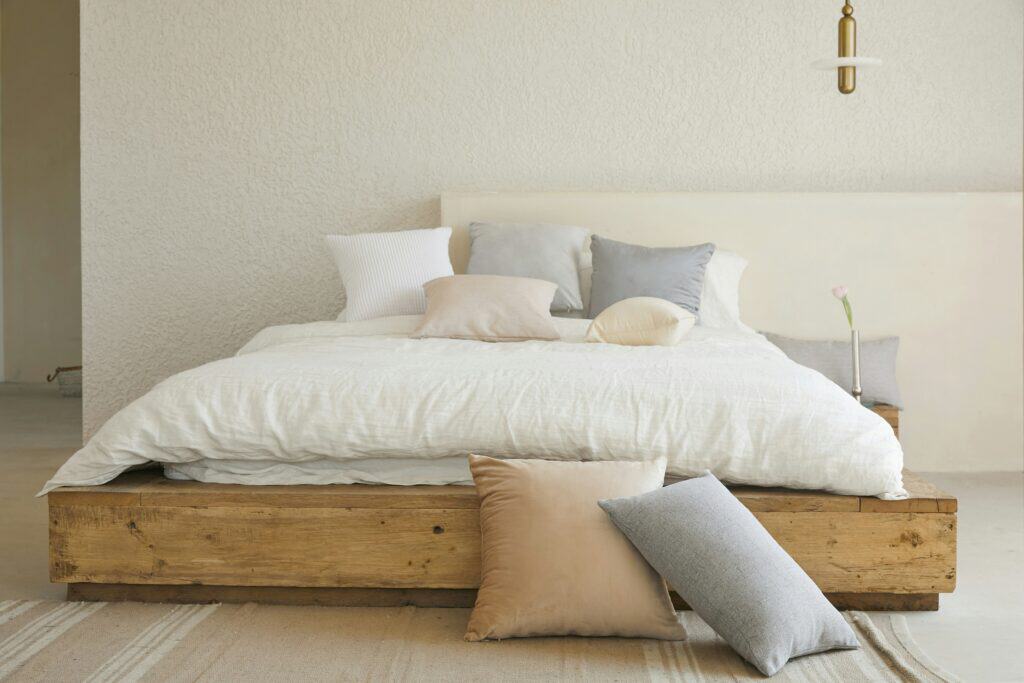 Made bed with white linen bedding and grey and blush cushions on a reclaimed wood frame