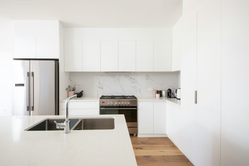 Minimal white kitchen with a marble splashback, stainless range and an island sink